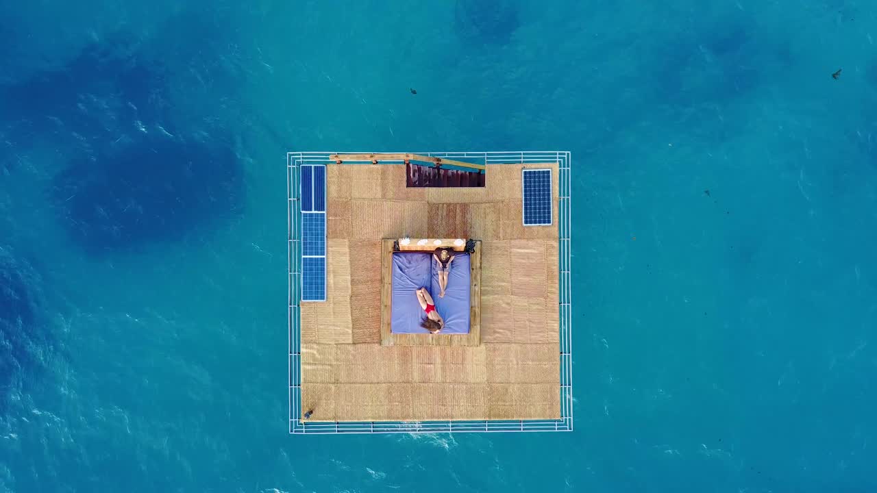 Aerial drone shot over the Manta Resort underwater hotel in Tanzania Africa with a man and woman lounging on the platform over the ocean