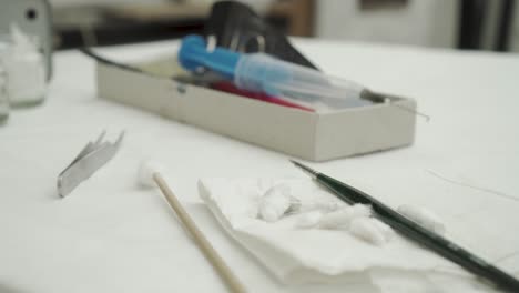 Closeup-of-laboratory-tools-on-table---tweezers,-cotton-wool,-paint-brush-and-injection-with-needle
