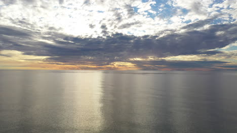 aéreo: volando hacia atrás sobre el mar báltico durante la hora dorada con un horizonte majestuoso con colores naranja y azul en el cielo