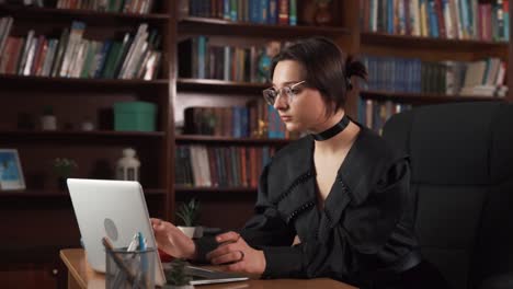 the girl is sitting at a table and working on a laptop, then she closes the laptop and sits there, lost in thought