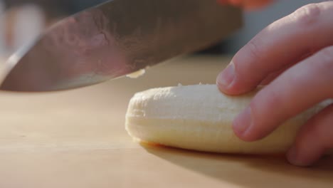 Schneiden-Sie-Von-Hand-Eine-Banane-Auf-Einer-Holzoberfläche