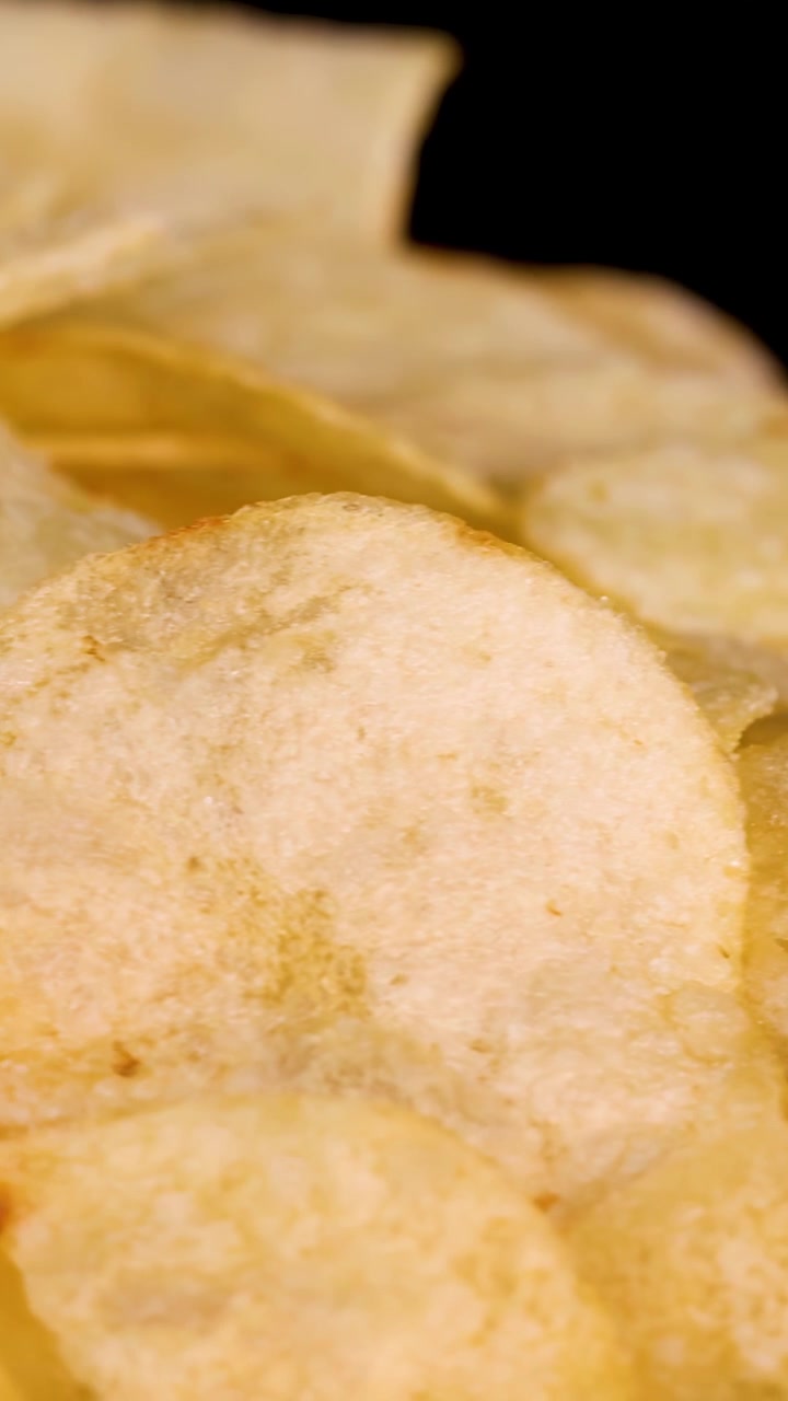 Golden potato chips rotate slowly under studio lighting, highlighting texture and crispness on black background