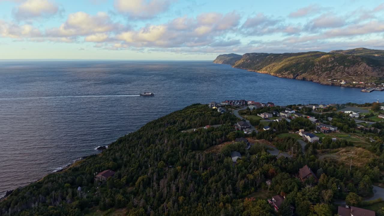 Aerial footage glides over the rugged shoreline of Portugal Cove in Newfoundland, revealing green hills, coastal cliffs and the blue expanse of the Atlantic Ocean