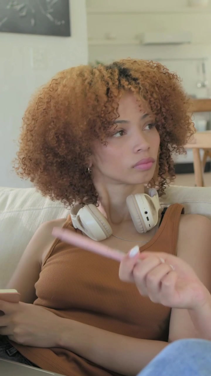 Video verticale: Donna che studia, in maglietta marrone, che accetta una penna rosa e prende appunti su un quaderno a casa.