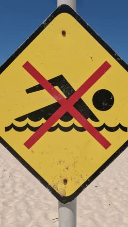 yellow sign warning against swimming due to danger