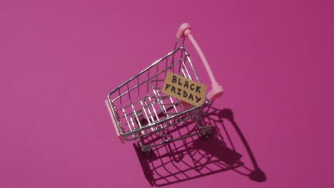 Video-of-black-friday-text-on-cardboard-in-shopping-trolley-on-pink-background