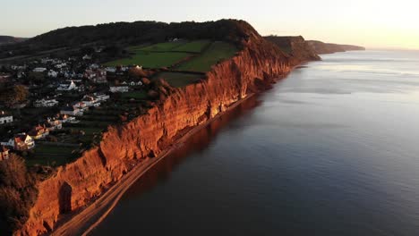 Antenne-Entlang-Der-Küste-Von-Sidmouth,-Die-Morgens-In-Goldenes-Sonnenaufgangslicht-Getaucht-Ist