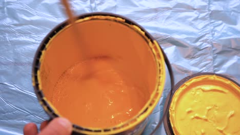 painter stirring yellow wall paint in a can with a stick.