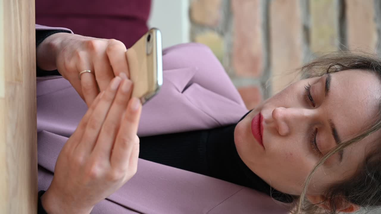 Close up of a woman in a pink blazer typing on her phone in a restaurant. Vertical