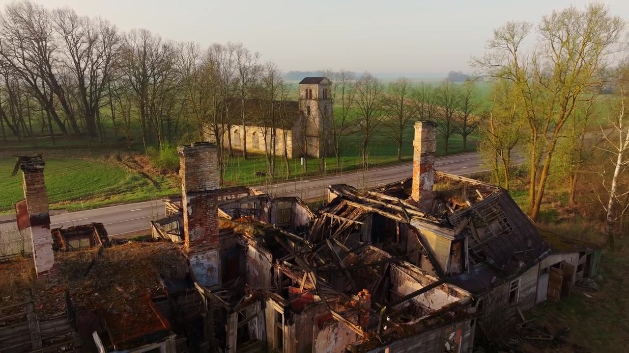 Charred ruins reveal Gluda Lutheran church beyond green farmland at spring dawn