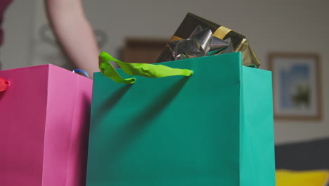 close up of man picking up gift wrapped presents in colourful bags with tag on table in lounge at home