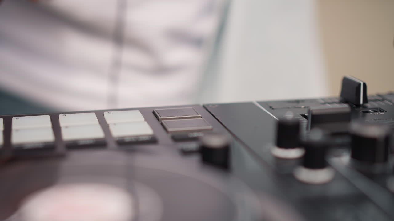 Closeup DJ controller black DJ hand mixing studio session focusing on tactile pads knobs jog wheel fader turntable male black DJ wearing white shirt manipulates pads and knobs to craft rhythm warm