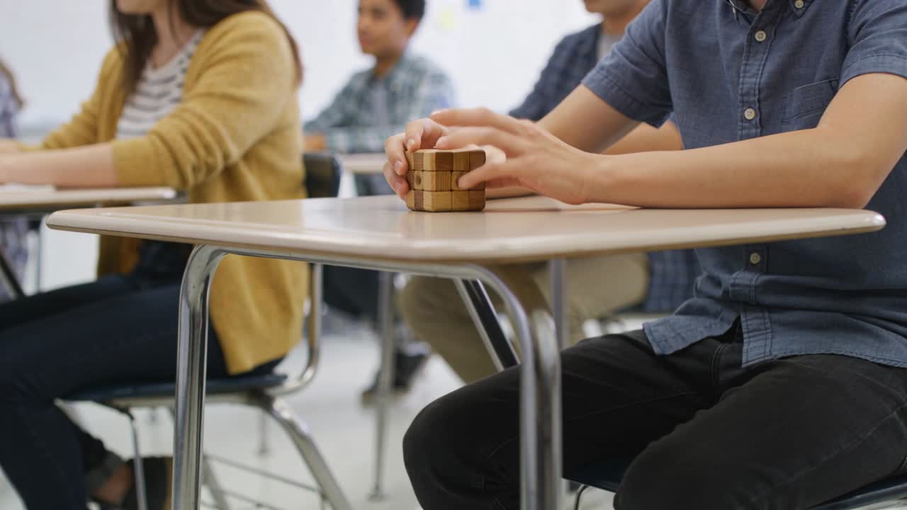 Video verticale: Uno studente con una maglietta blu che gira un puzzle di legno in classe, osservando un cubo assemblato.