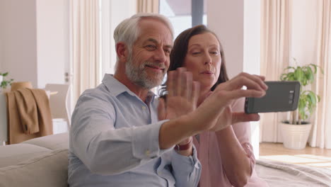 Feliz-Pareja-De-Mediana-Edad-Usando-Un-Teléfono-Inteligente-Teniendo-Video-Chat-Lanzando-Un-Beso-A-Sus-Nietos-Disfrutando-De-La-Comunicación-En-Línea-Relajante-Casa-De-Retiro