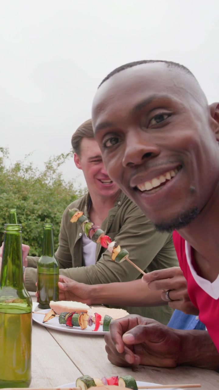 Verticale video: Vriend die fles optilt, man in rood shirt gebarend met spiesjes aan tafel, ruimte voor tekst