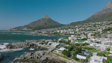 Fly-above-sea-coast.-Vacation-buildings-in-tourist-destination.-Pointed-Lions-Head-mountain-against-clear-blue-sky-in-background.-Cape-Town,-South-Africa