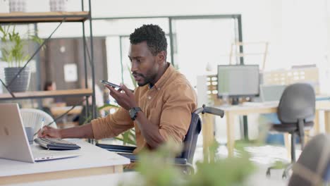 Behinderter-Afroamerikanischer-Geschäftsmann-Im-Rollstuhl,-Der-In-Zeitlupe-Am-Tisch-Auf-Dem-Smartphone-Spricht