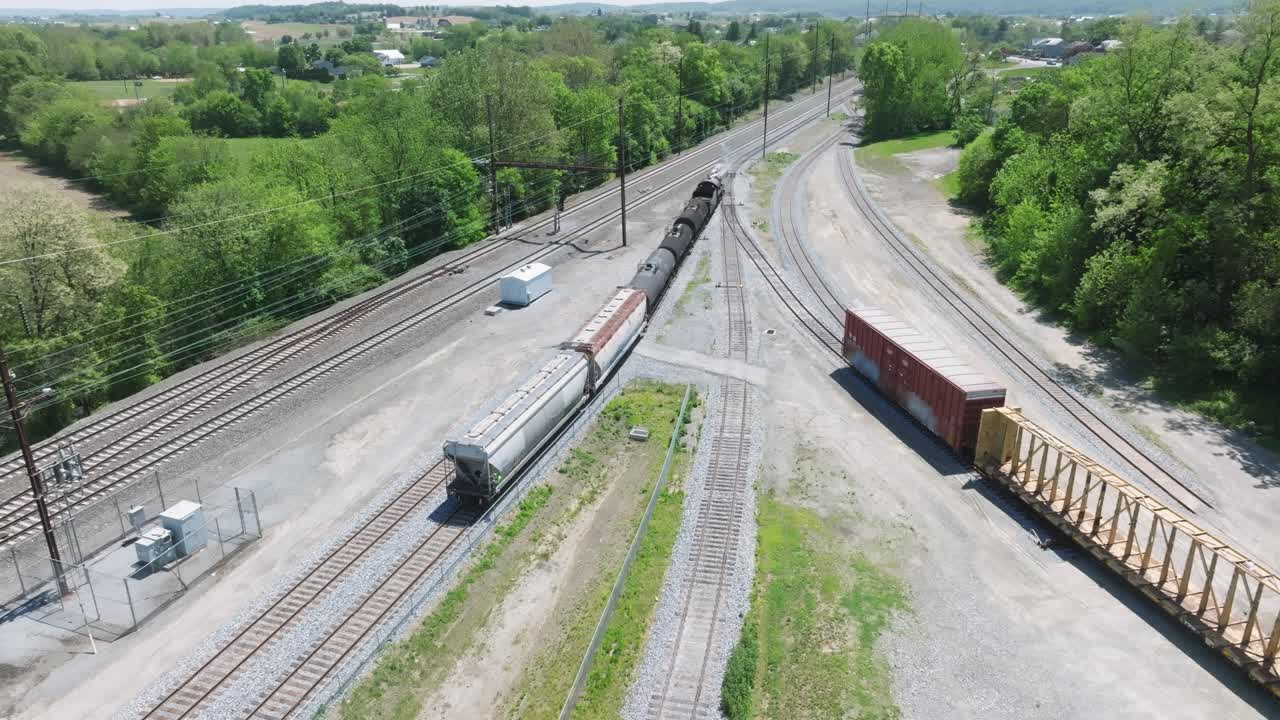 A vintage steam freight train makes its way backing up in yard performing switching operations moving steadily along the railway tracks in a peaceful countryside setting