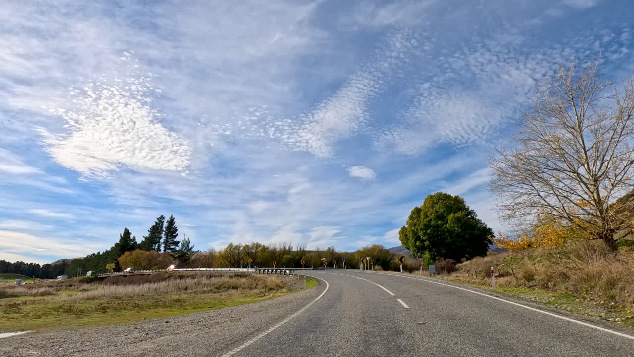 A serene drive through Queenstown's autumn landscape, showcasing vibrant foliage, clear skies, and winding roads under bright sunlight