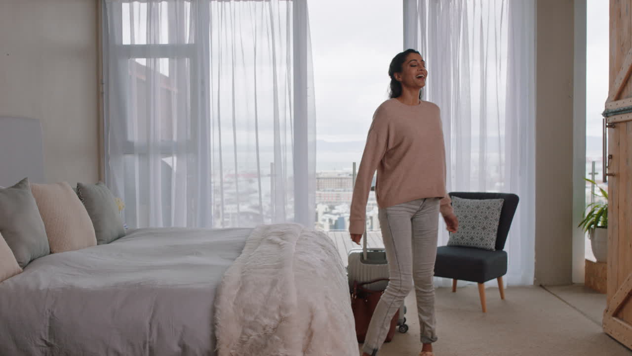 행복한 젊은 여성이 침대에 뛰어 성공적인 여행 여행 후 휴식을 취하고 호텔 방에서 독립적인 라이프 스타일 자유를 즐기고 있습니다.