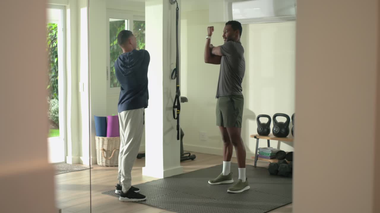 After demonstration African American trainer and male client warming shoulders on mat in home gym