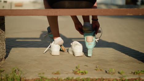 back view of woman putting right leg into roller skate while other skate rests on left leg, left leg partially out of sneaker, seated on bench with warm sunlight casting soft shadows