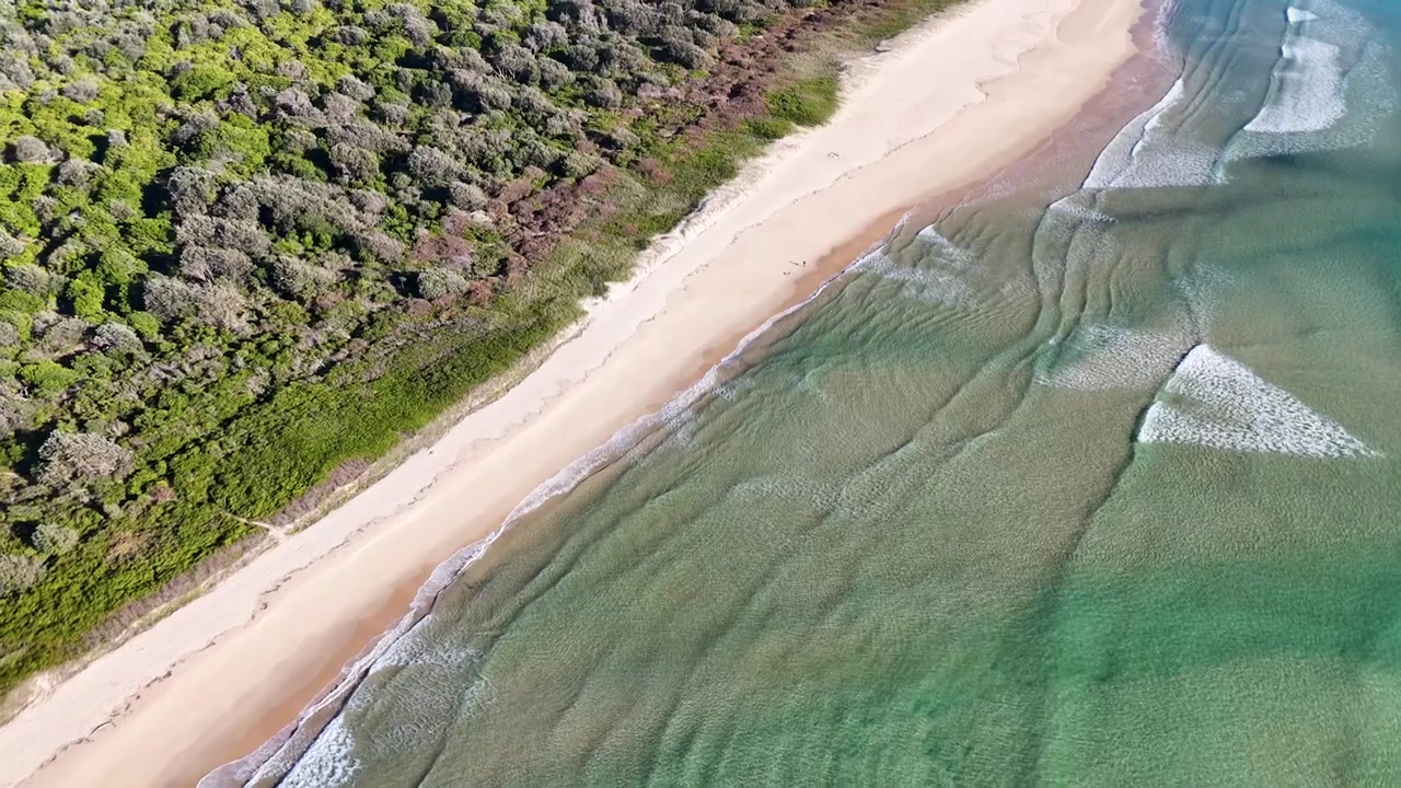 High-angle drone shot of turquoise ocean waves breaking on a sandy Australian coastline.