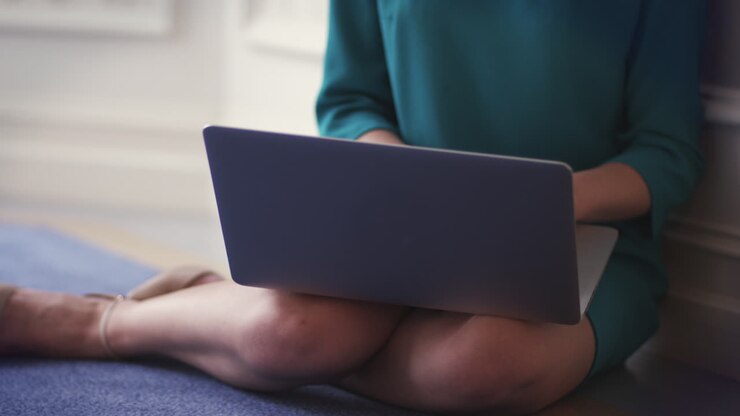 Imprenditrice seduta sul pavimento in camera e lavorando al computer portatile