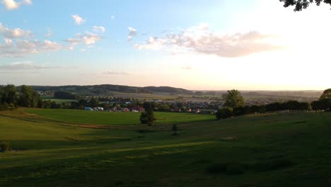 Moving-over-foliage-towards-green-valley-with-houses-at-dusk