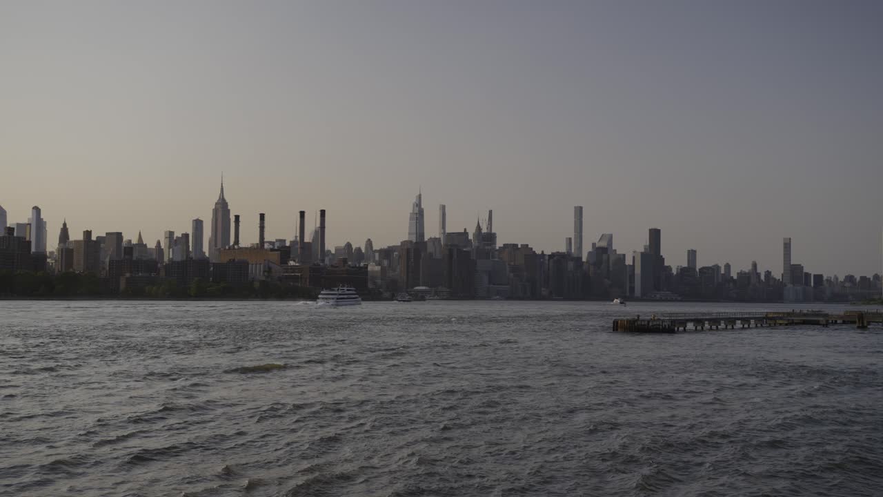 Panning wide shot of the New York City skyline at sunset, featuring glowing skyscrapers and warm light reflecting off the buildings, captured from across the river.