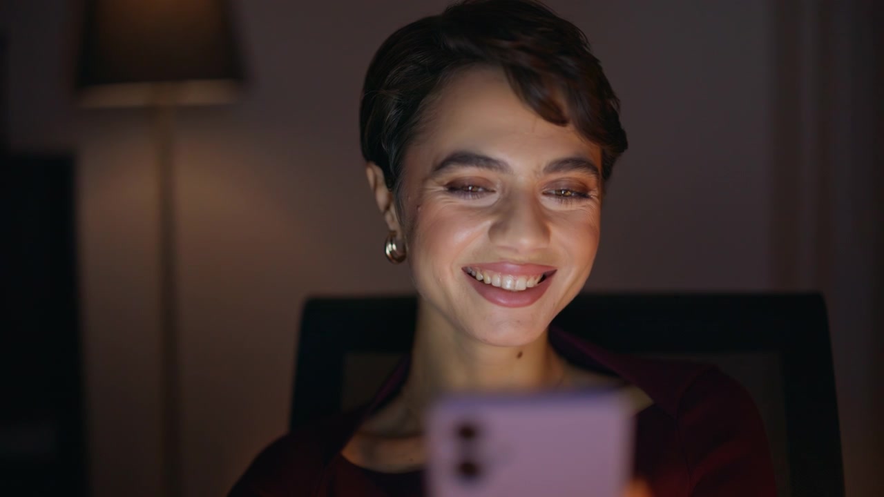 Donna che legge lo smartphone a casa la sera. Primo piano di una donna felice che scorre il telefono di notte.