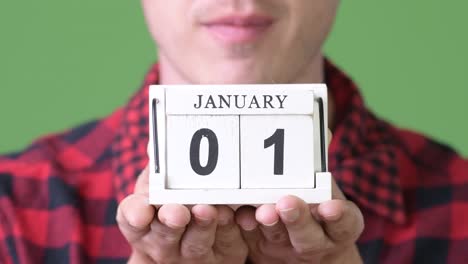 young happy man showing calendar block against green background