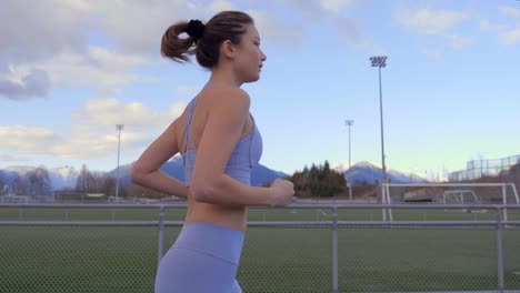 tiro de seguimiento de perfil de cámara lenta, mujer atlética trota en la pista mirando hacia la derecha