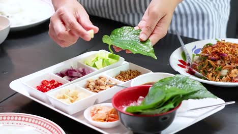 hands assembling traditional thai miang kham leaf wraps with ingredients