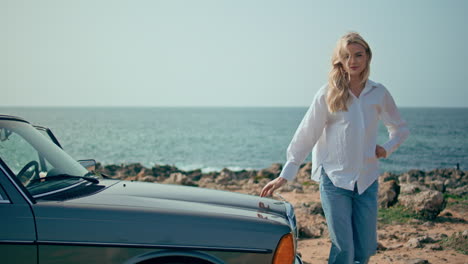 modelo elegante posando coche retro en la costa de verano. mujer de pie en la playa soleada.