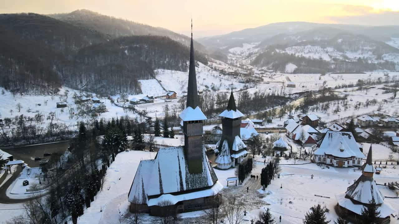 Lot z drona nad monastyrem Barsana w Rumunii. Główny kościół i inne budynki, goście, wzgórza pokryte nagim lasem i śniegiem, zima