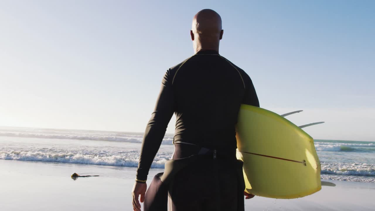 Uomo anziano afroamericano che cammina con una tavola da surf in spiaggia