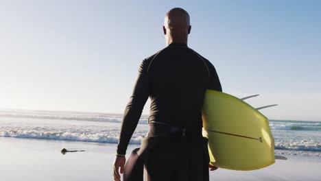 senior african american man walking with a surfboard at the beach