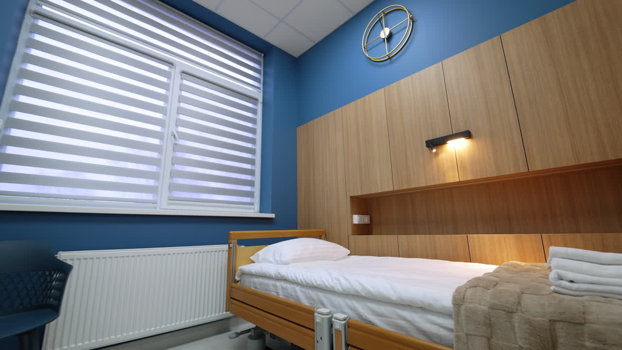 Patiëntenkamer met houten meubels en blauwe wanddetails. Minimalistisch ziekenhuisinterieur gericht op een verstelbaar bed, kasten met houtnerf en een design wandklok.