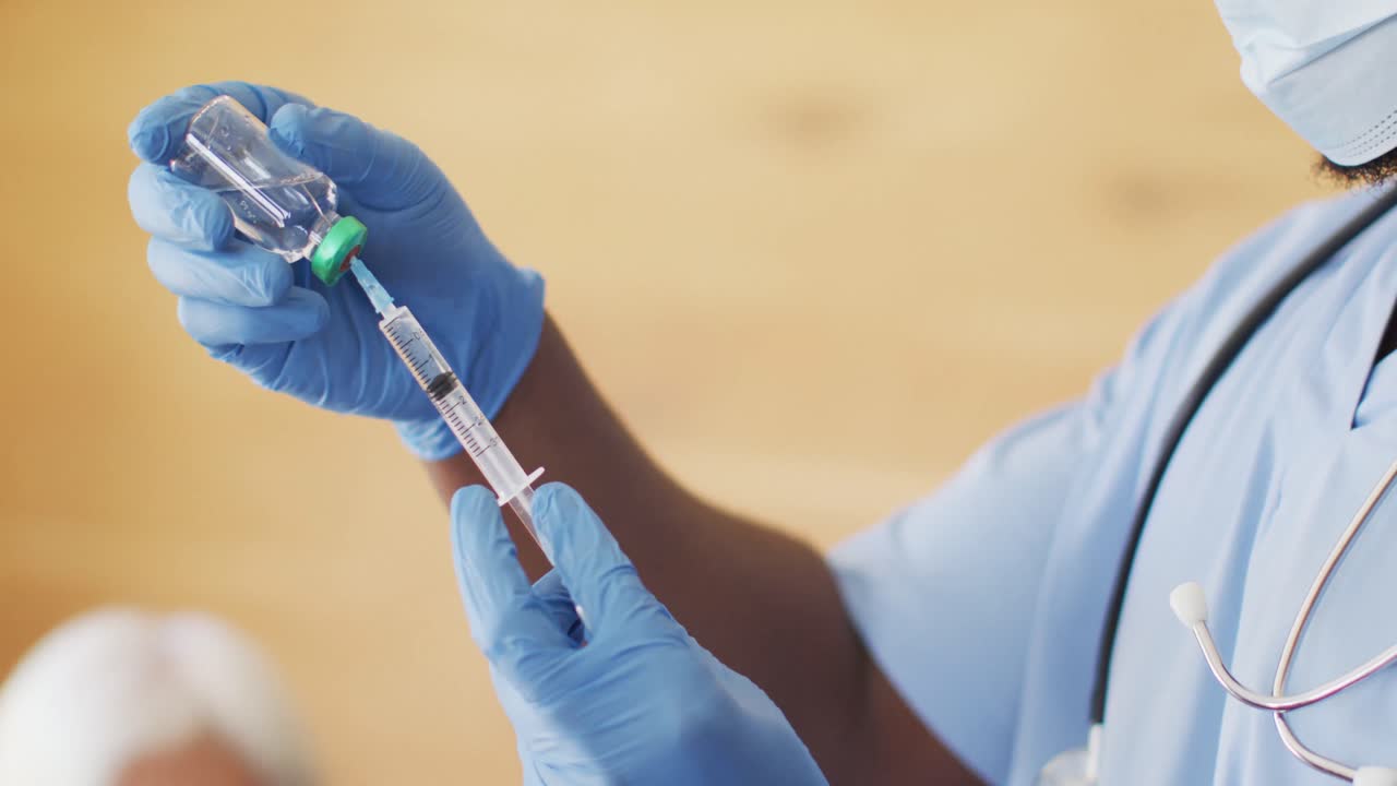 Video of african american male doctor in face mask preparing vaccine
