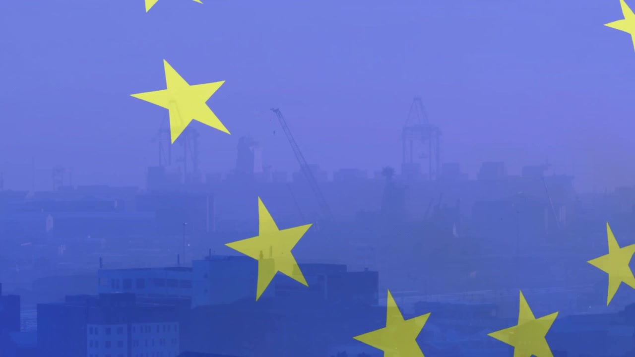 Bandiera dell'UE che sventola, apparendo da sinistra su uno skyline nebbioso con gru che rappresentano l'unità.
