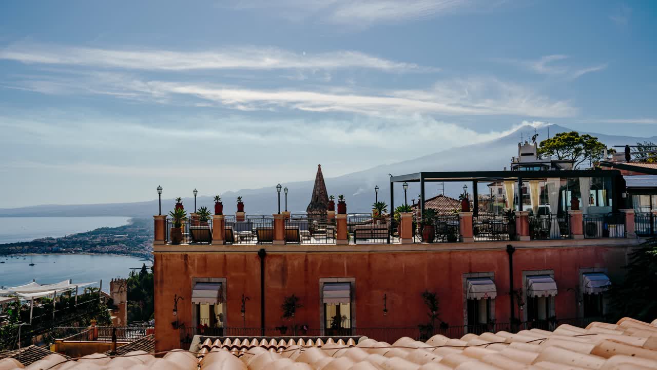 View to rooftop terrace in Taormina with Mount Etna in the background. Timelapse video of volcano smoking in a sunny summer day.