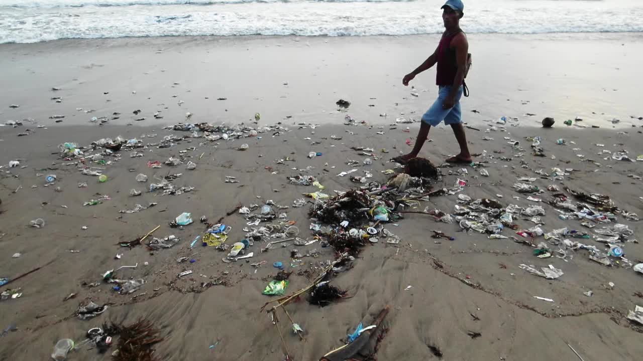 gente local caminando en la orilla de bali mientras las olas arrastran basura plástica del océano, costa contaminada