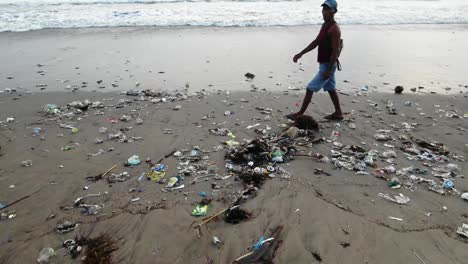 local people walking on the shore on bali as waves washing out plastic trash from the ocean, polluted coastline