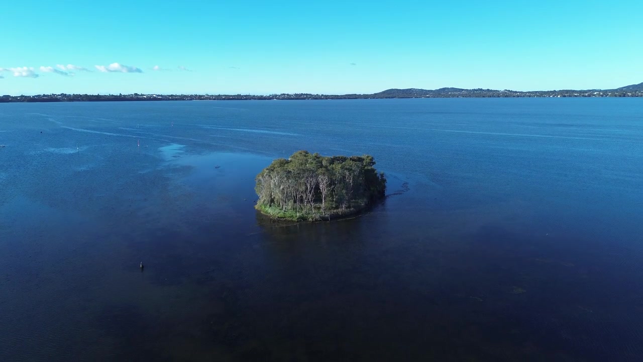 Paisaje aéreo con dron de matorrales y entorno de isla cubierta de árboles en el sistema acuático del lago Tuggerah, con un promontorio de pueblo rural en el horizonte en Chittaway Point, Costa Central, Australia, turismo de naturaleza