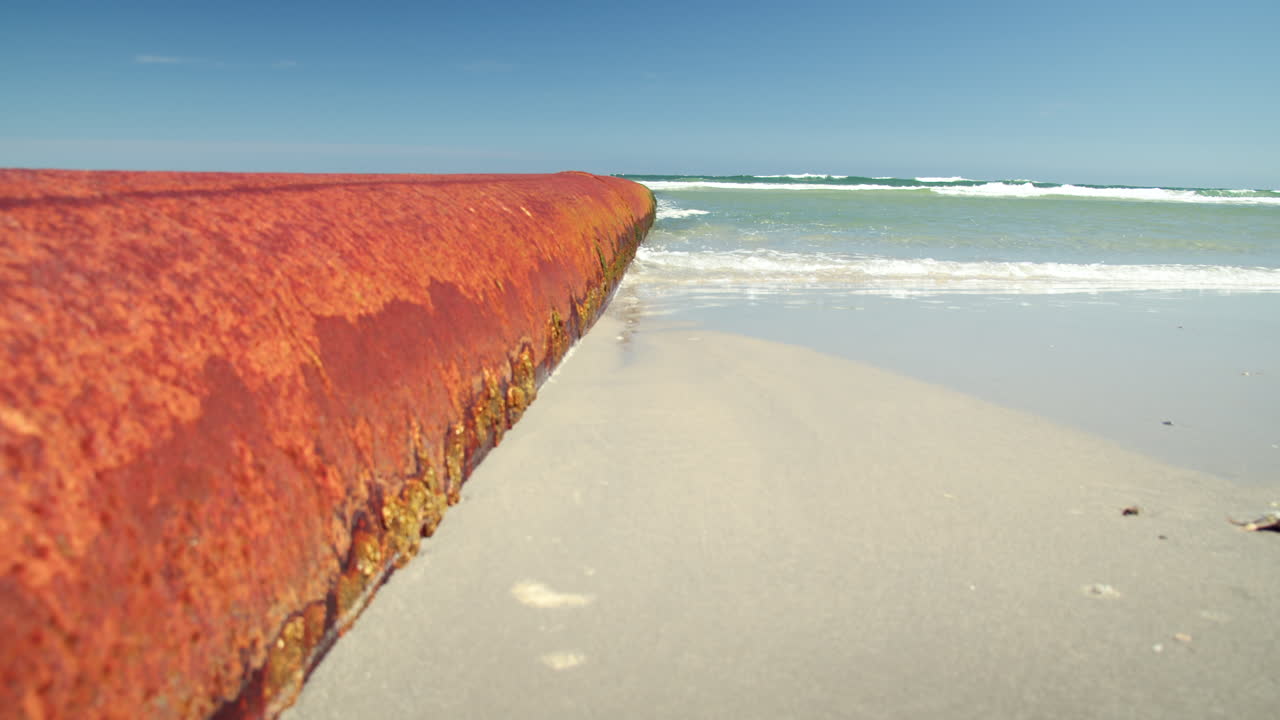 Waves Splash Along Large Orange Rusty Pipe in Slow Motion