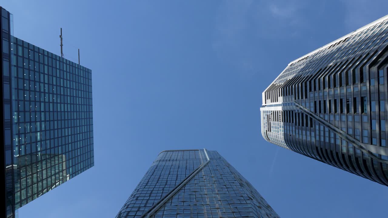 Laag camerastandpunt van een moderne glazen wolkenkrabber in het financiële district van Frankfurt met blauwe lucht en omringende hoogbouw.