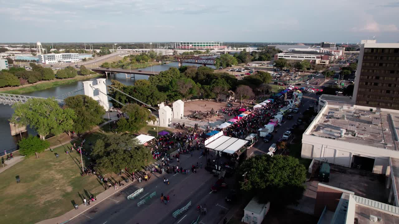 4K parallax drone footage of the Waco Suspension Bridge during the Día de los Muertos festival, capturing colorful decorations, vibrant crowds, and city scenery