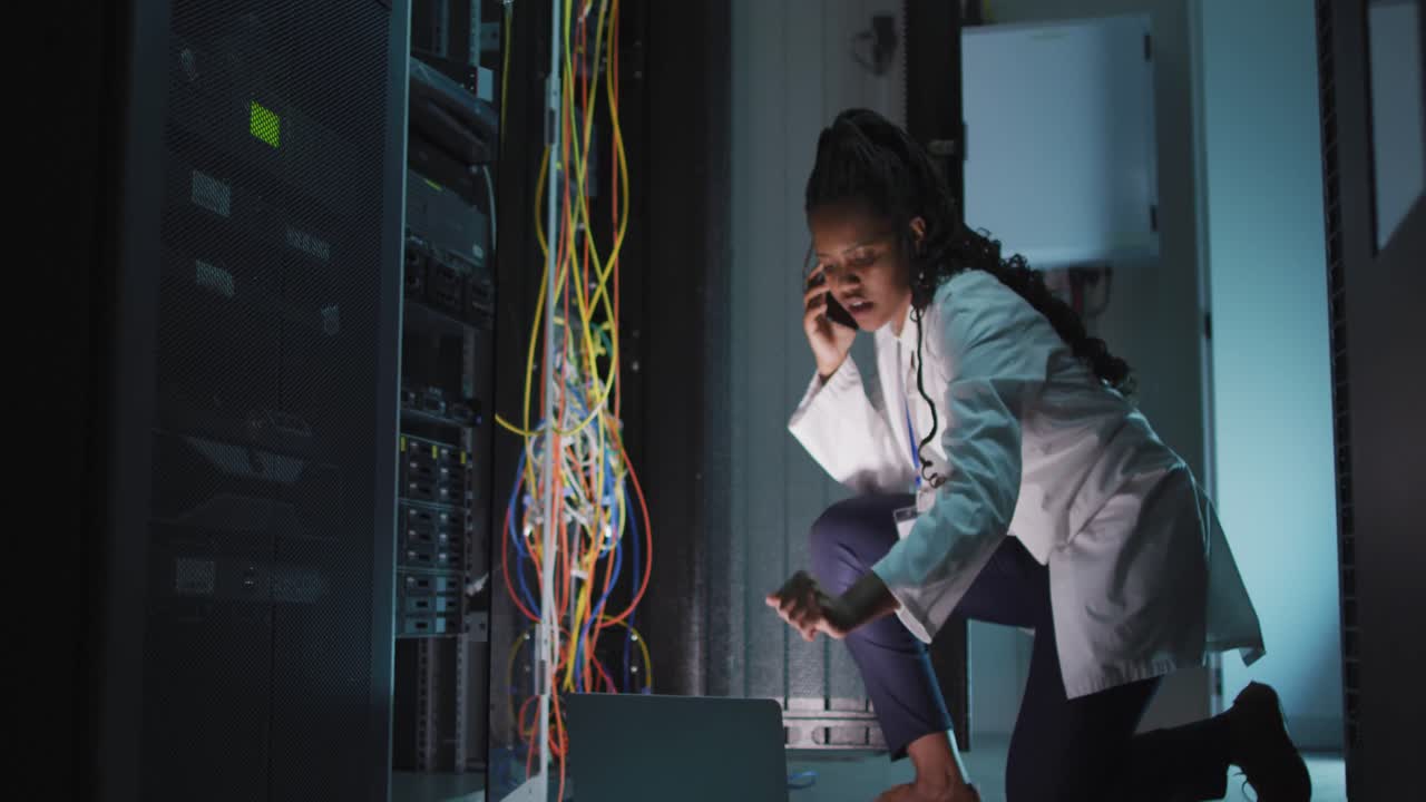 African american female computer technician using laptop working in business server room