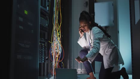 African-american-female-computer-technician-using-laptop-working-in-business-server-room